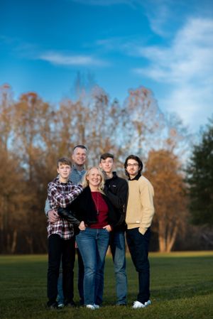 Family portrait of five people standing together outdoors with autumn trees in background.