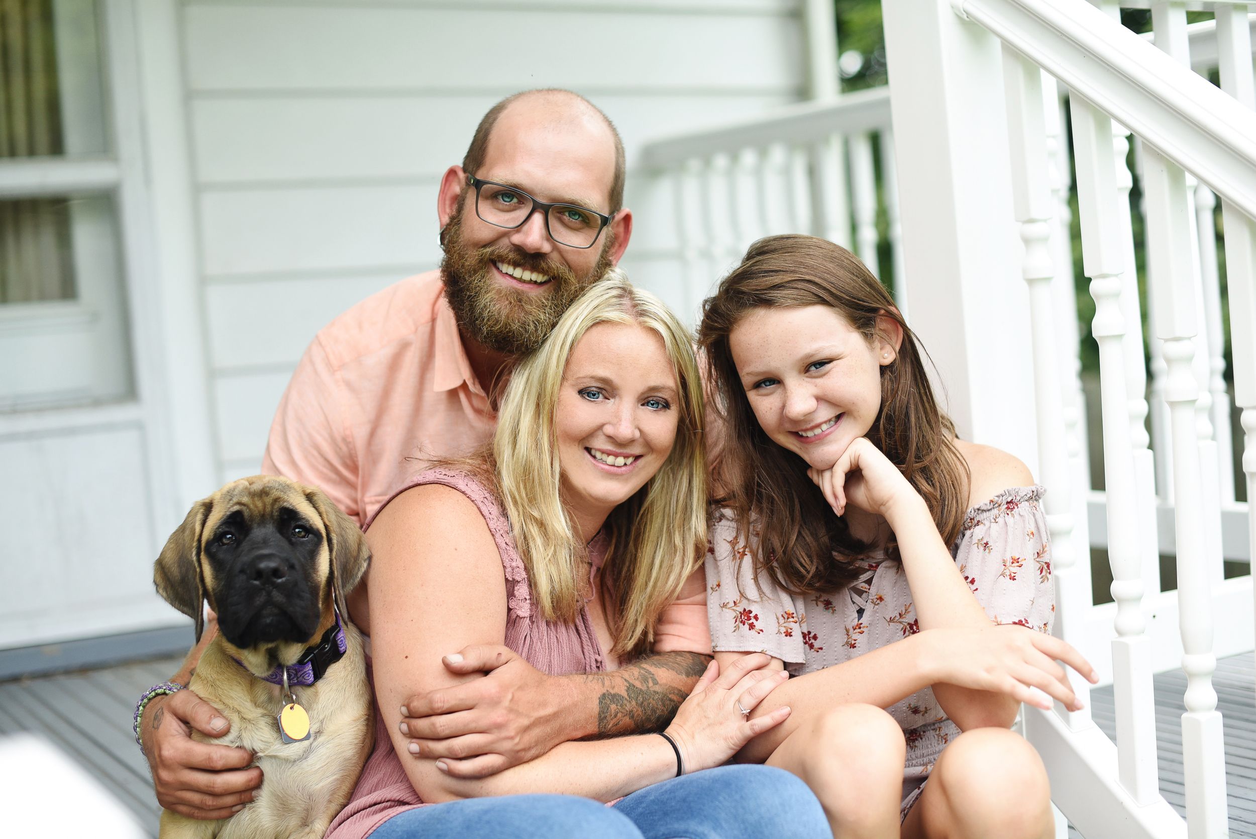 Family with pug dog poses casually on white porch steps during summer portrait session.