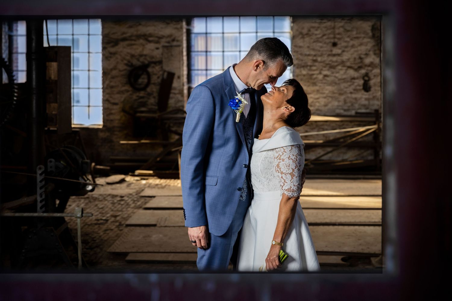 Romantic wedding photo of couple in rustic industrial venue with window light.