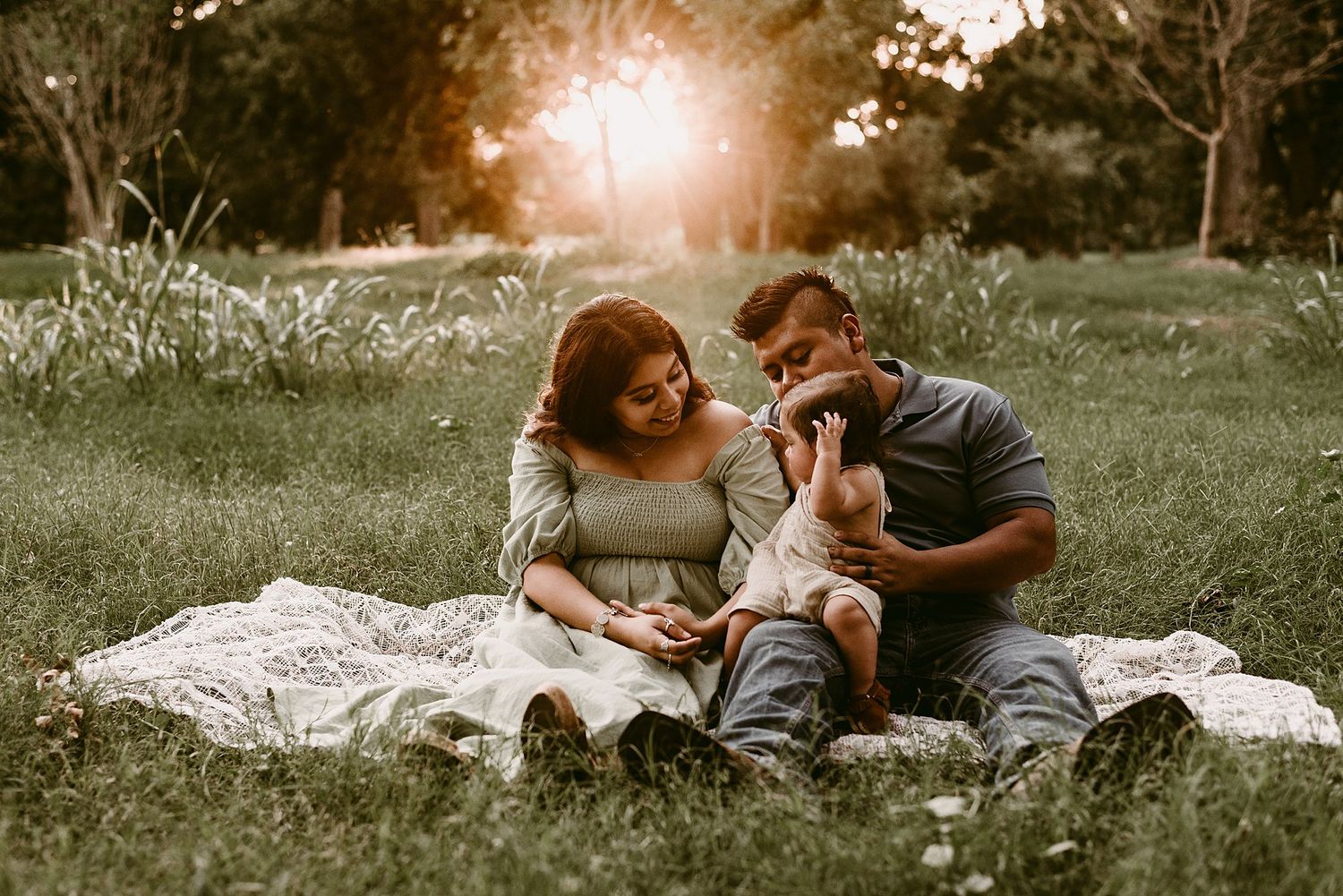 Family shares intimate moment together on picnic blanket in sunlit park during golden hour.