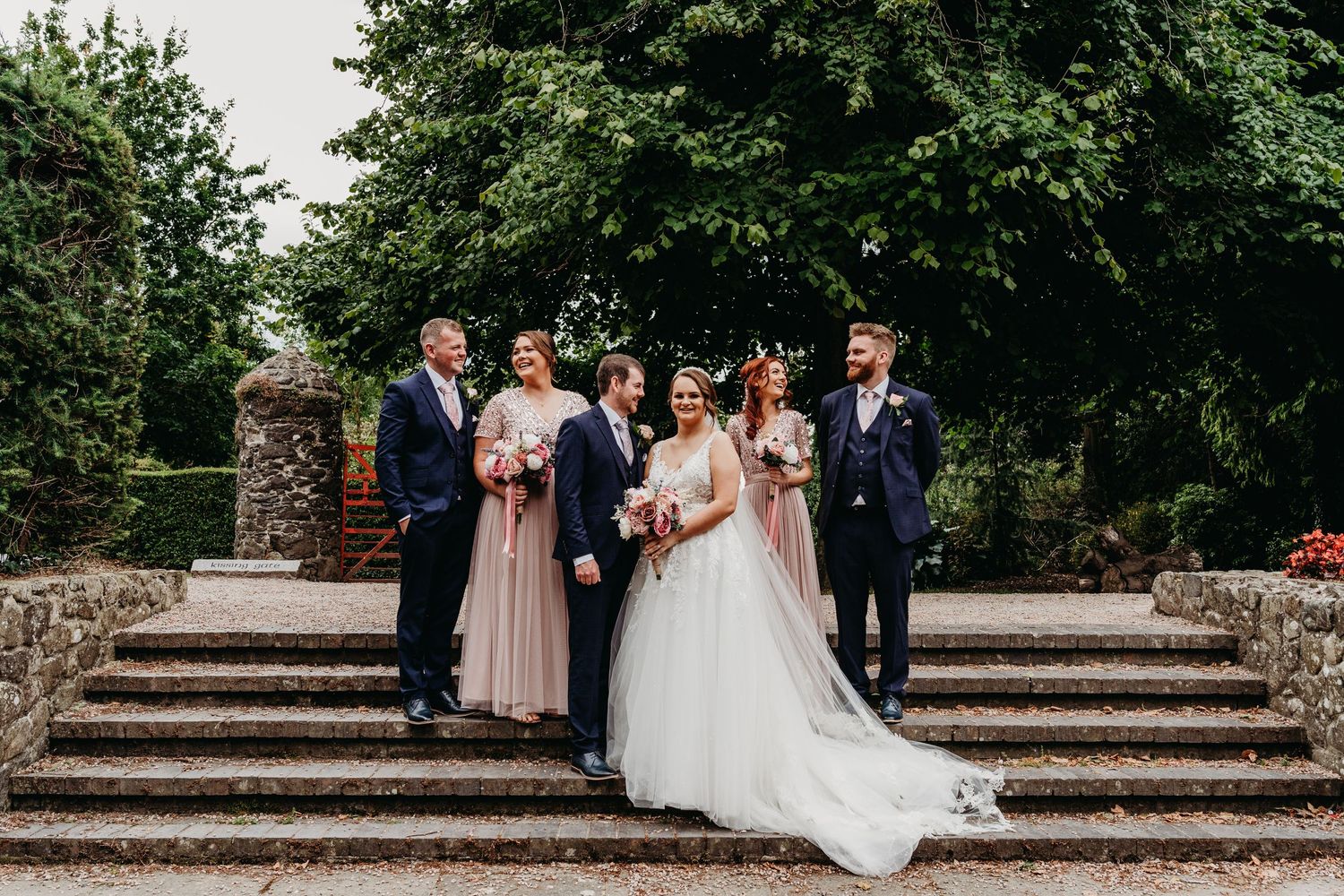 Bridal party, full of smiles, standing on steps in Tannaghmore Gardens.