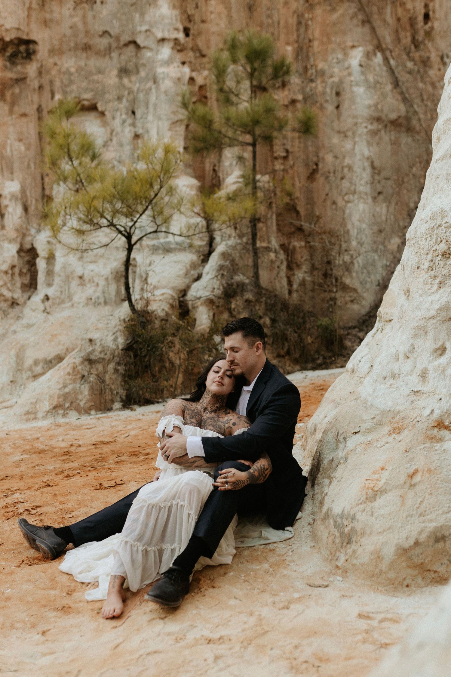 A tender moment between a couple sitting by limestone cliffs in formal attire.
