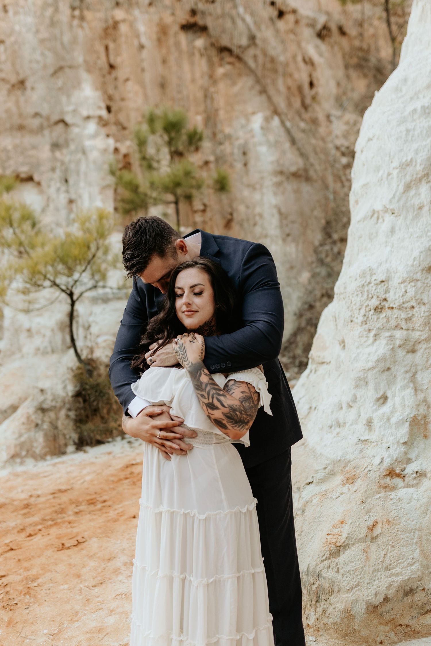A romantic embrace between a couple in formal attire against white limestone cliffs and desert landscape.