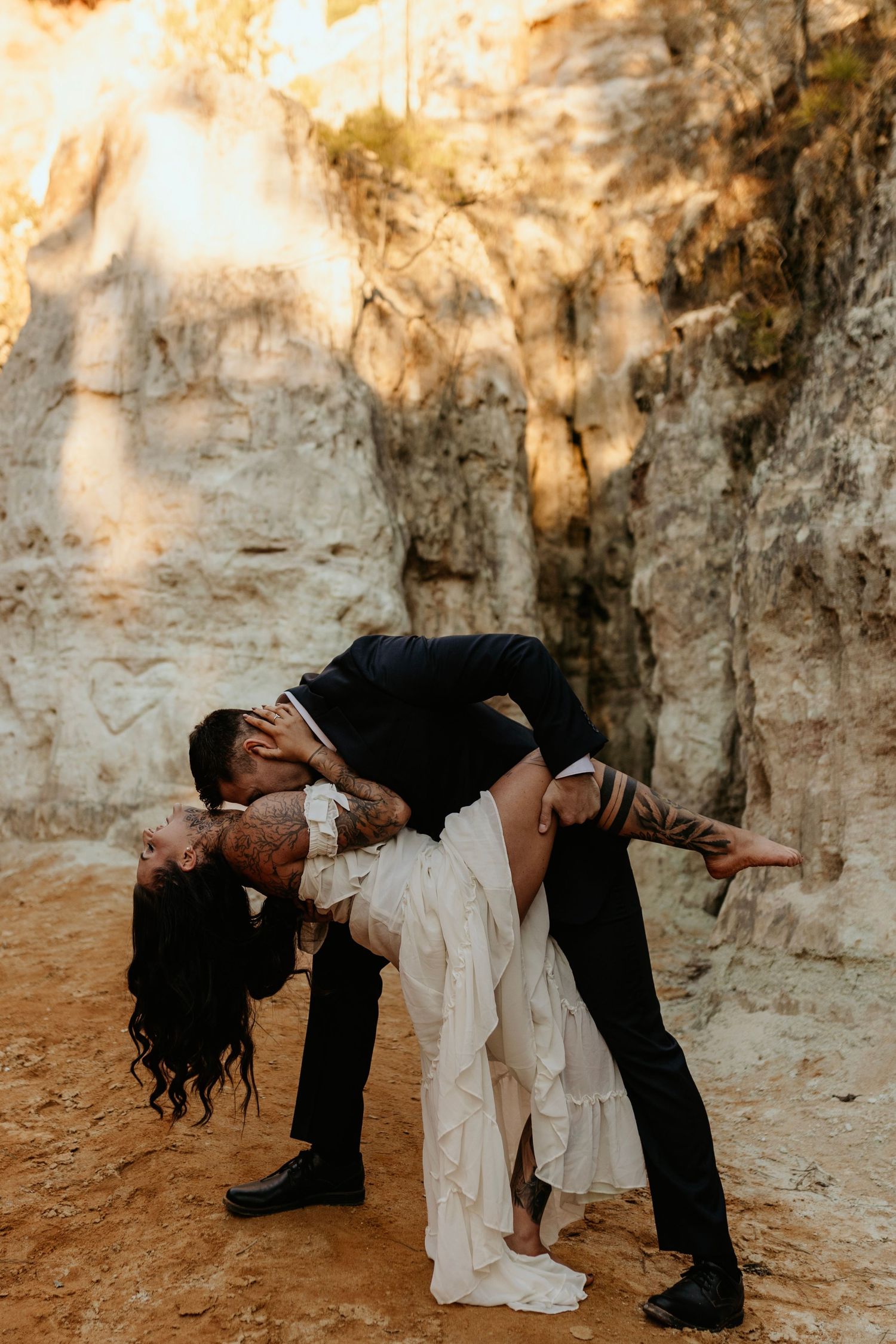 A dramatic dip pose between towering limestone walls in warm sunlight.