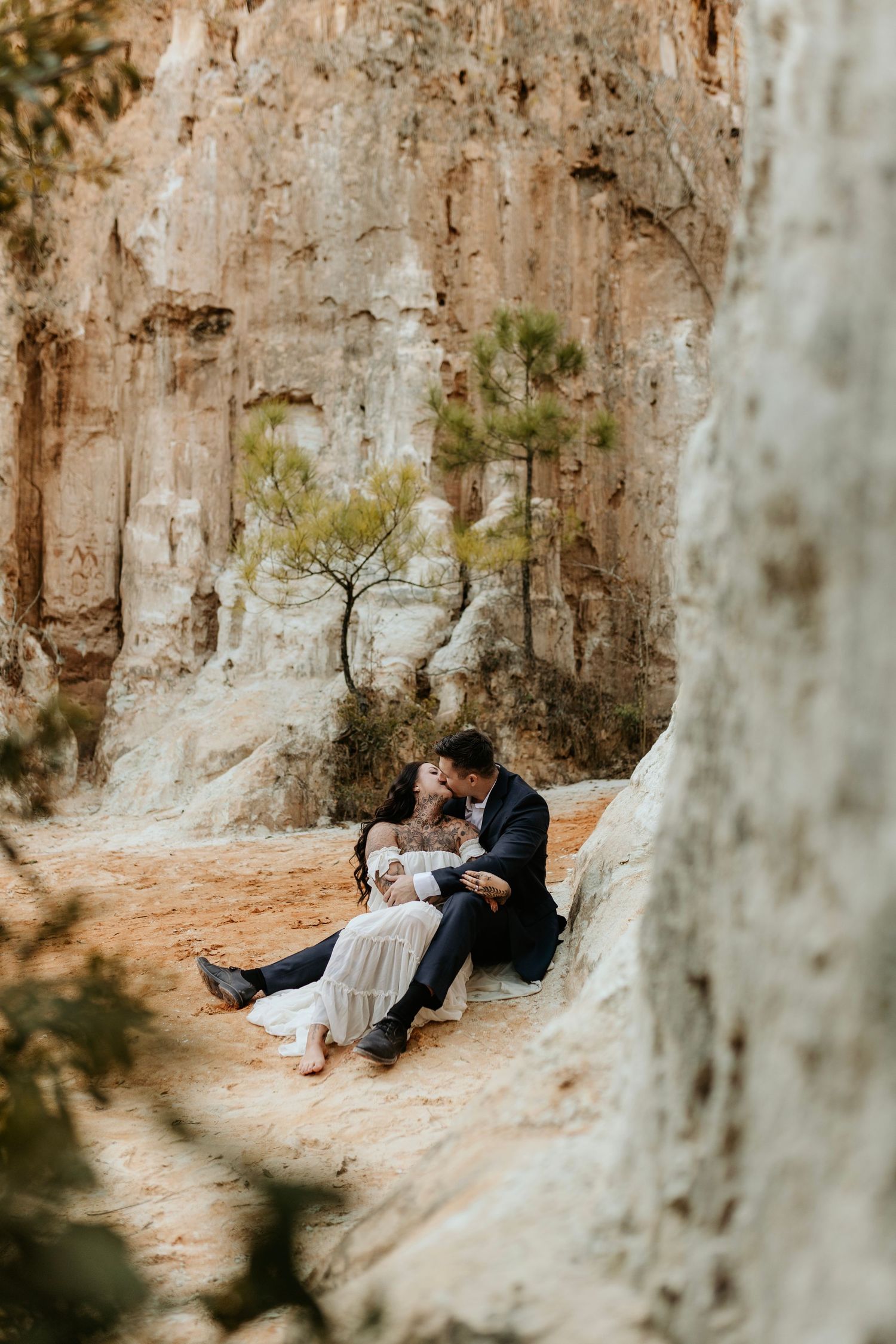 Couple in formal wear relaxing against white rock formations in a desert setting.