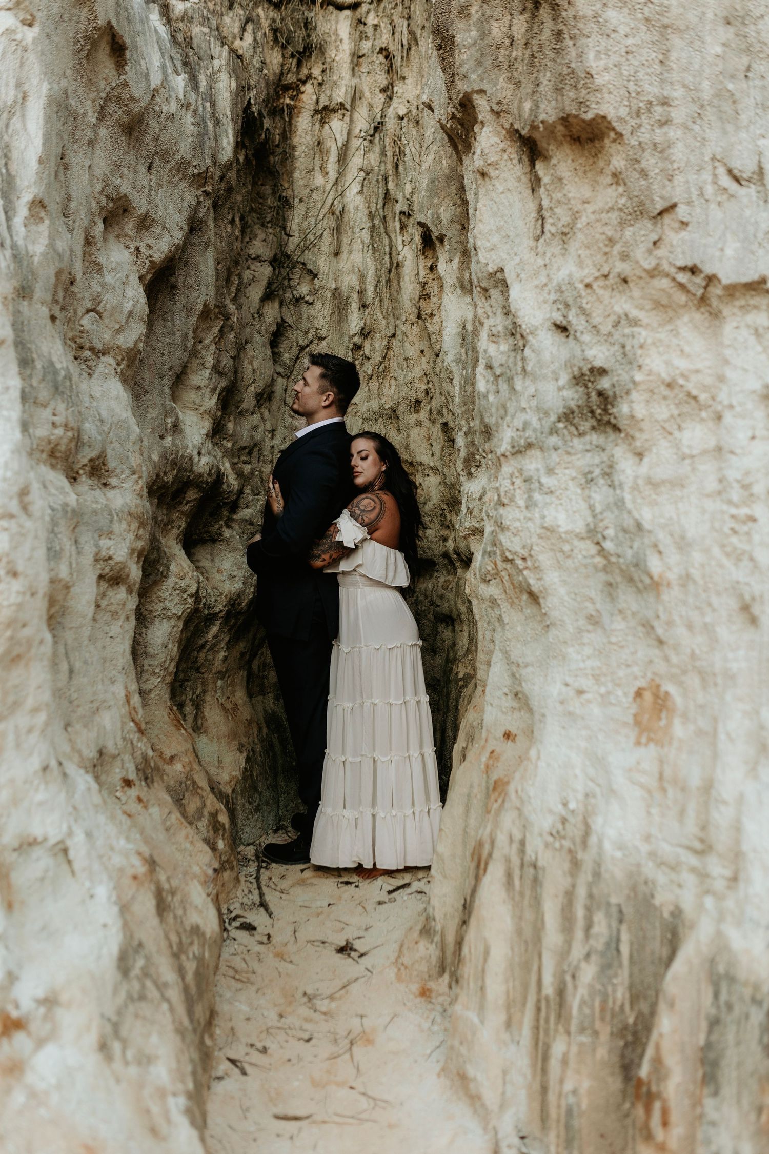 A loving pose against dramatic white limestone walls in natural lighting.