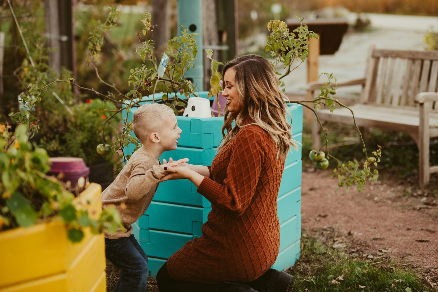 Parent and child share tender moment in garden setting with colorful rain barrels.