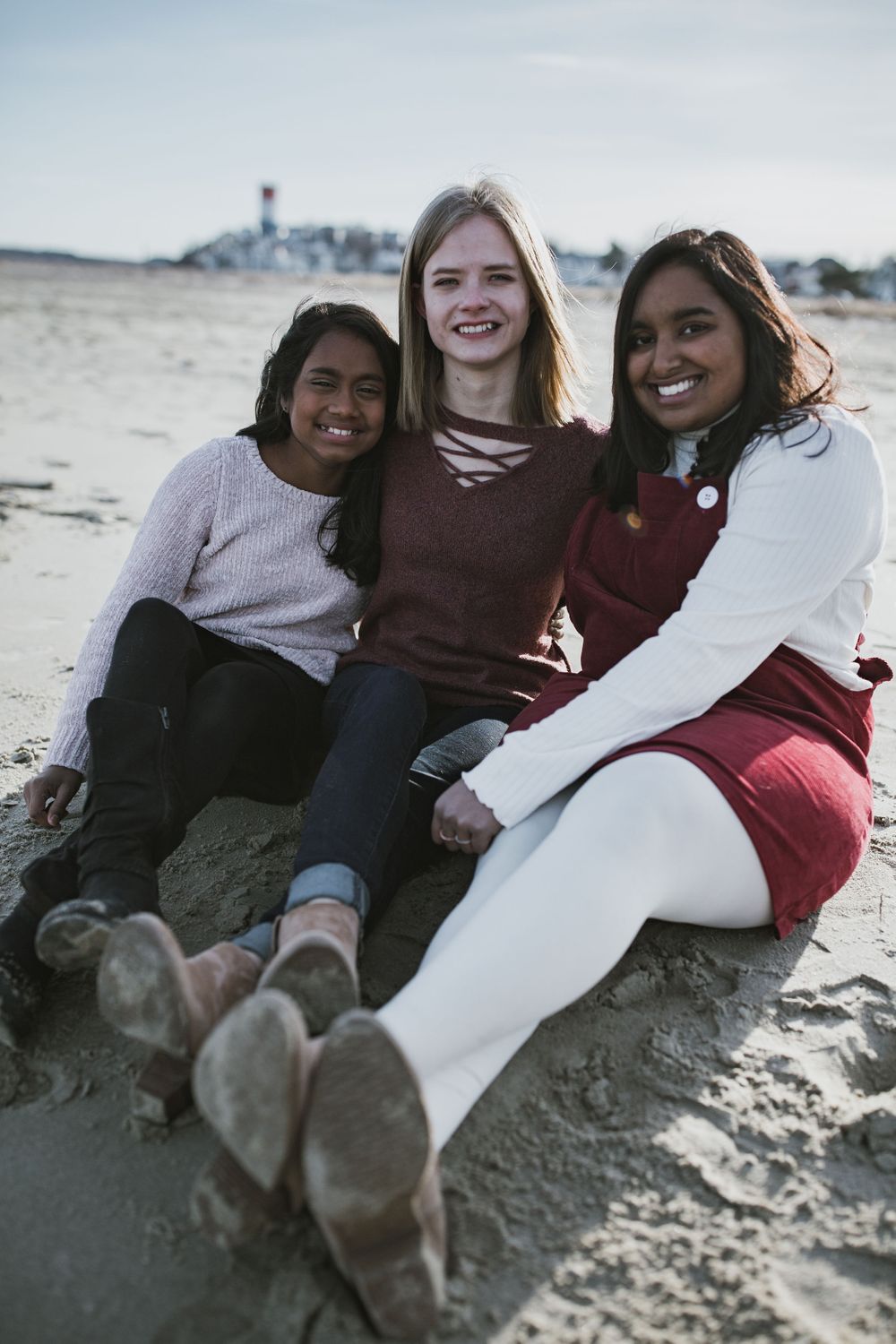 photo of three adopted sisters, sitting on the beach in the sand laughing with their arms around each other