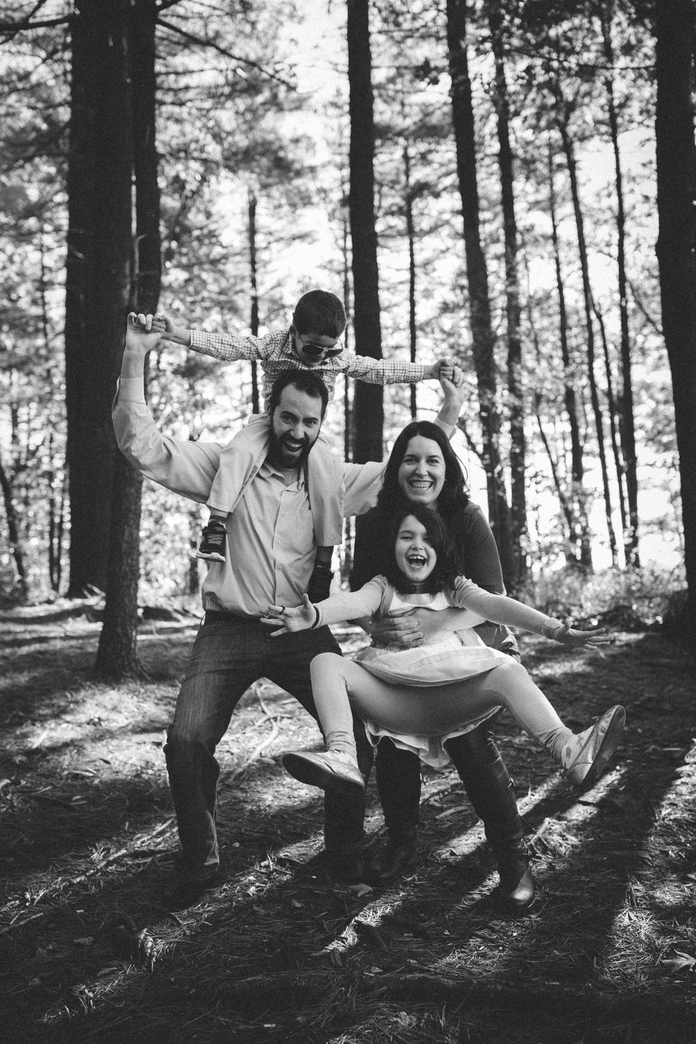 a funny family photo in the woods, parents are holding the kids and all are making funny faces