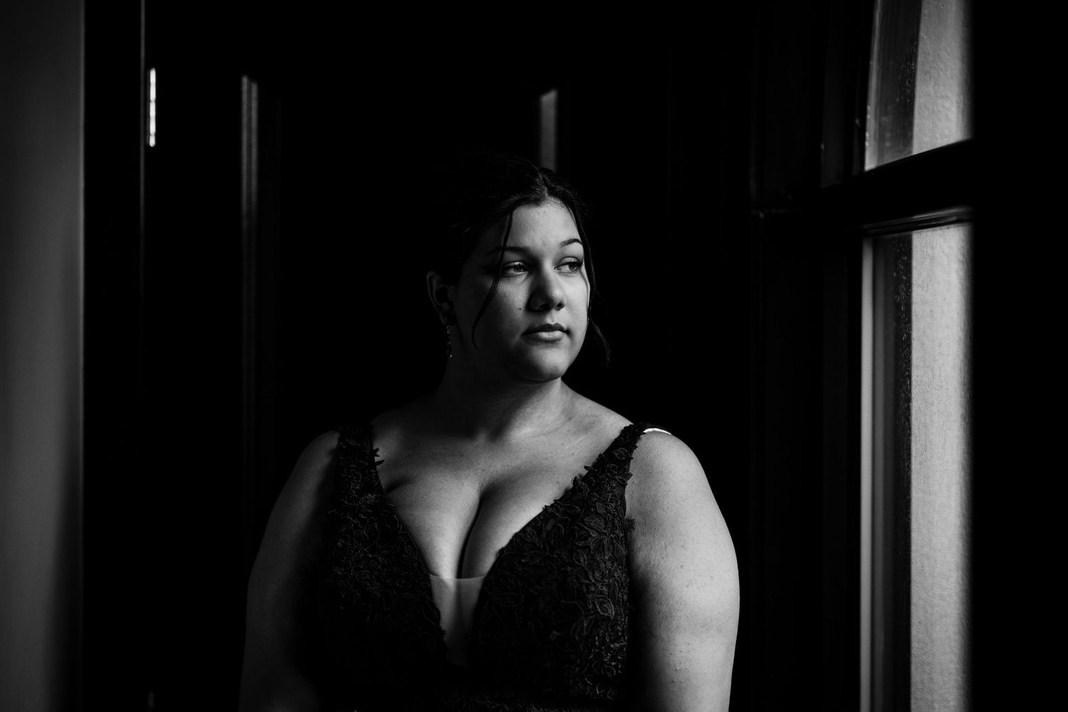 Dramatic black and white portrait showing a person in a lace dress near a window.