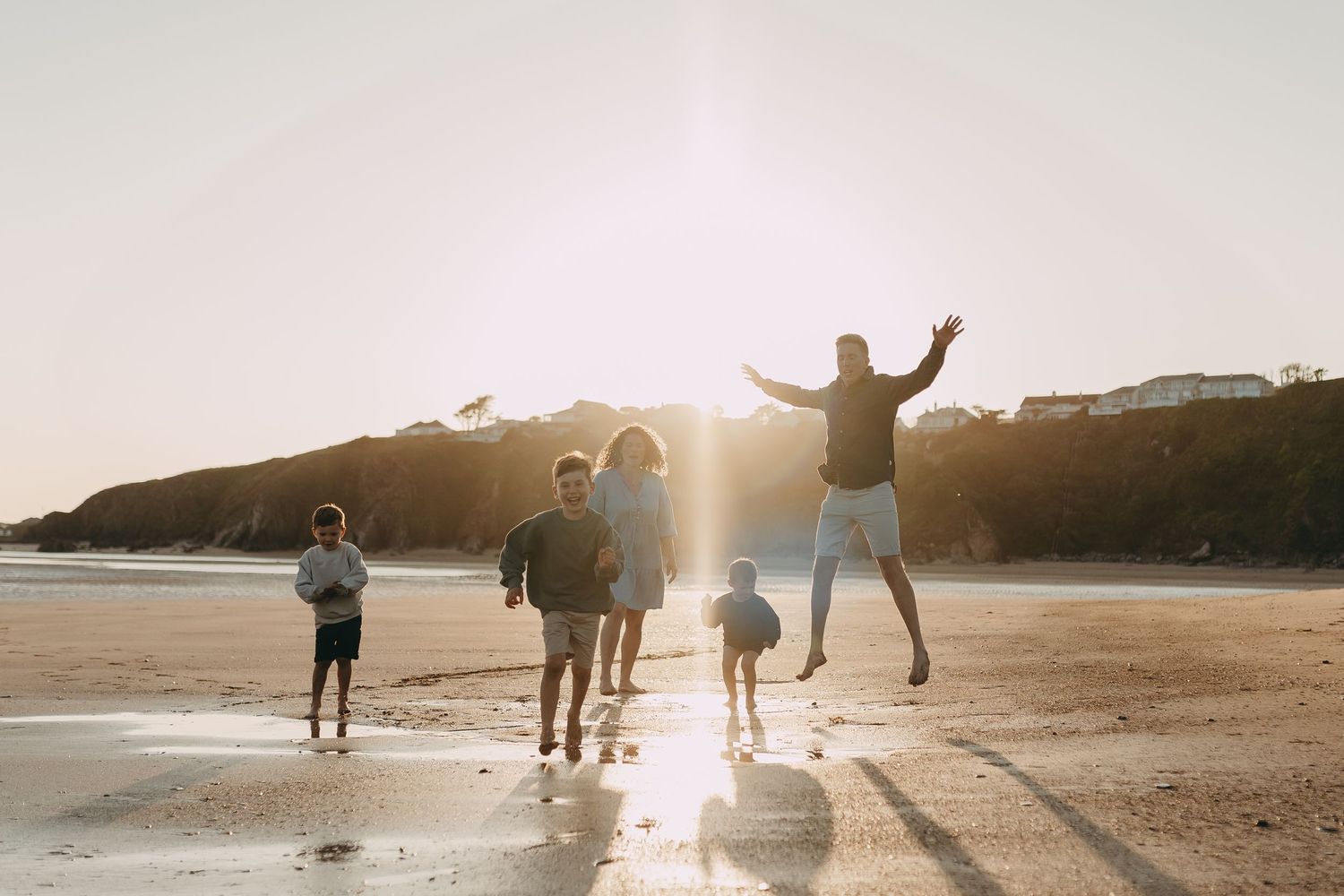 Silhouette of family playing and jumping on beach during golden sunset.