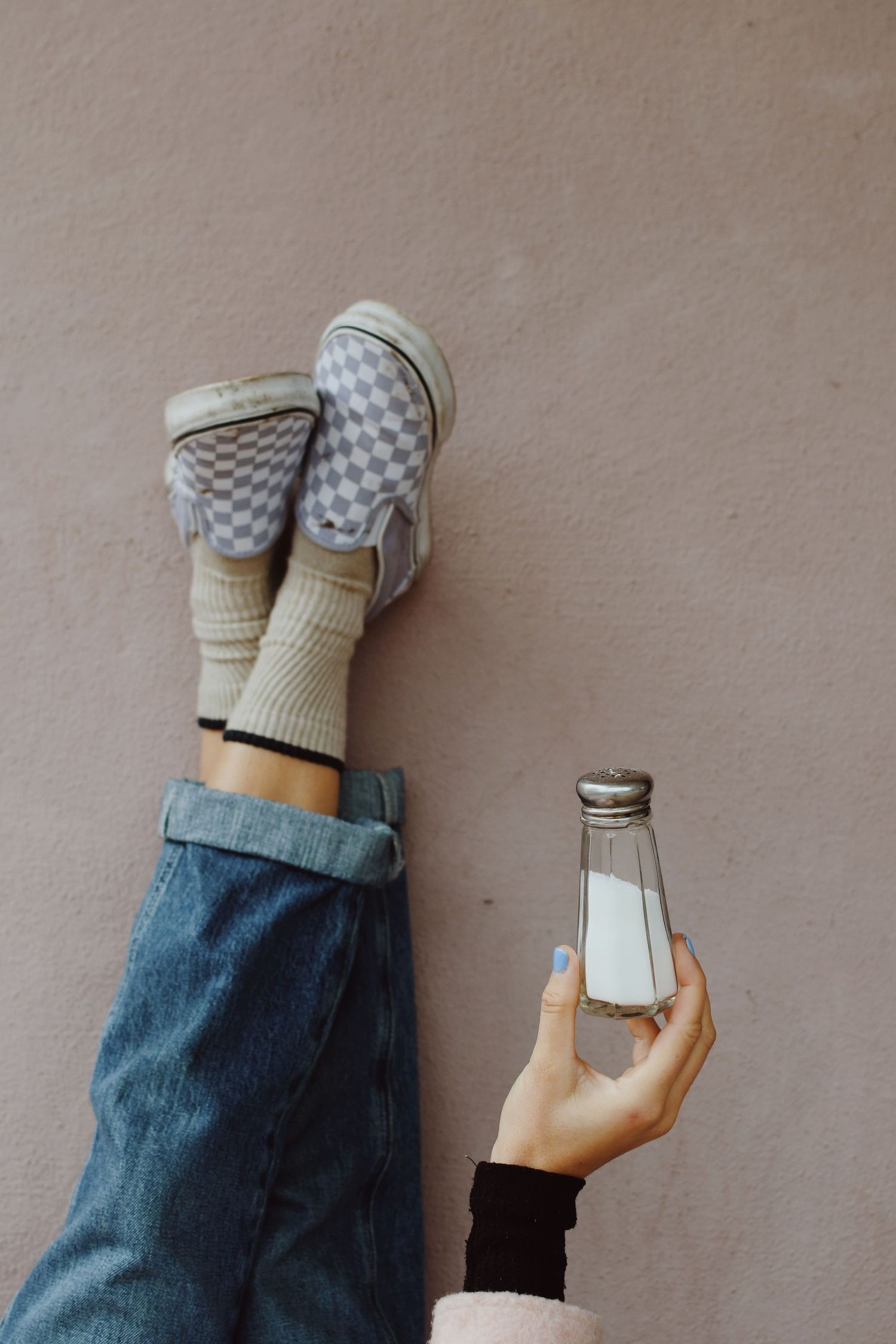 Person wearing checkered socks and jeans holding a glass milk bottle against pink wall.