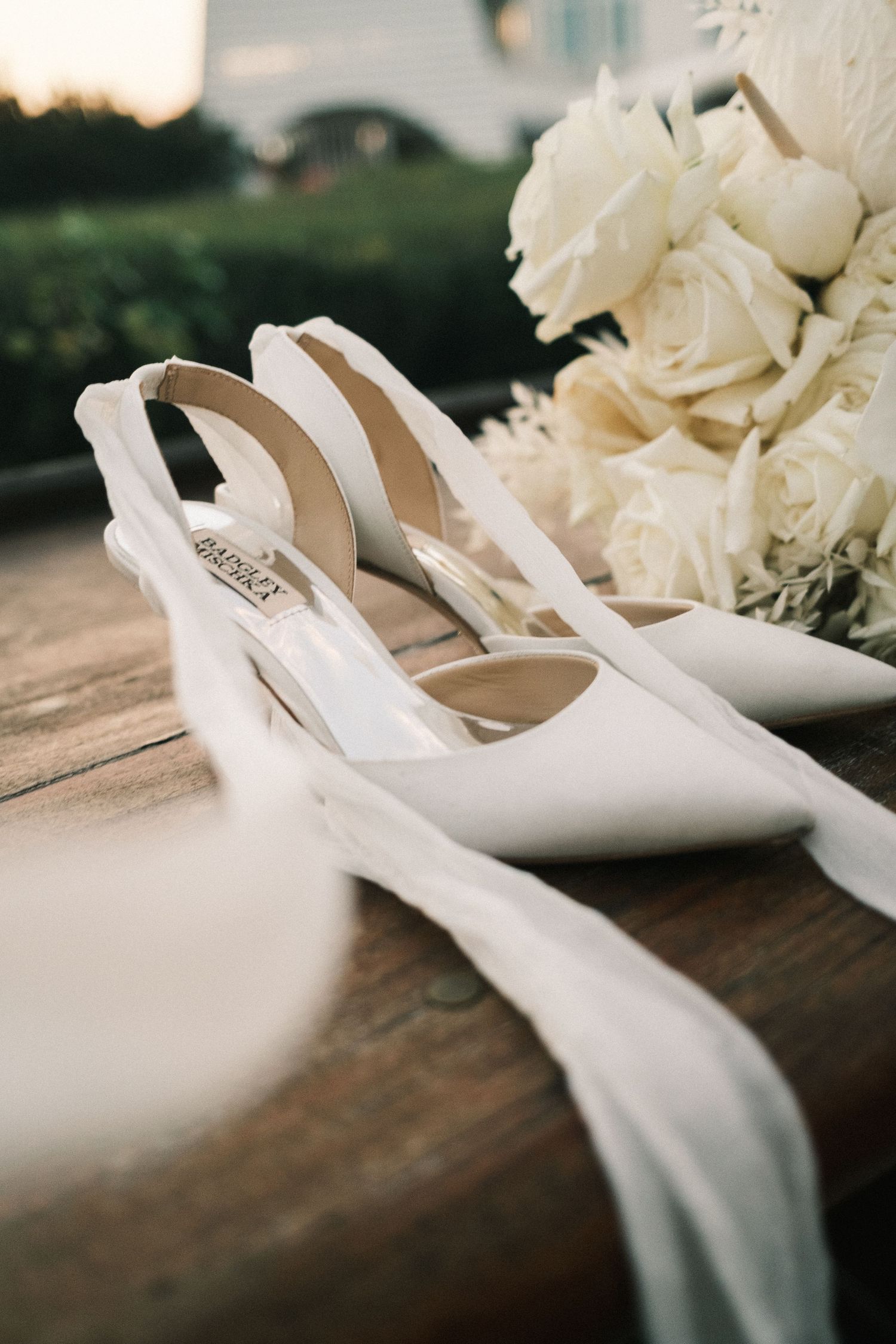 White bridal shoes arranged with roses on wooden surface.