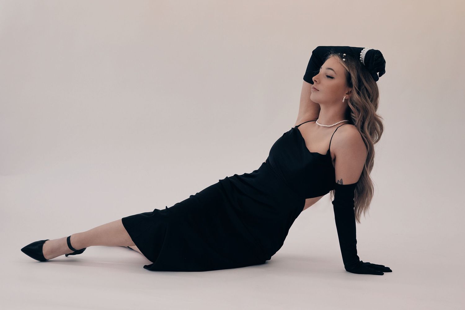 A glamour portrait of someone in a black dress posing on a light background.