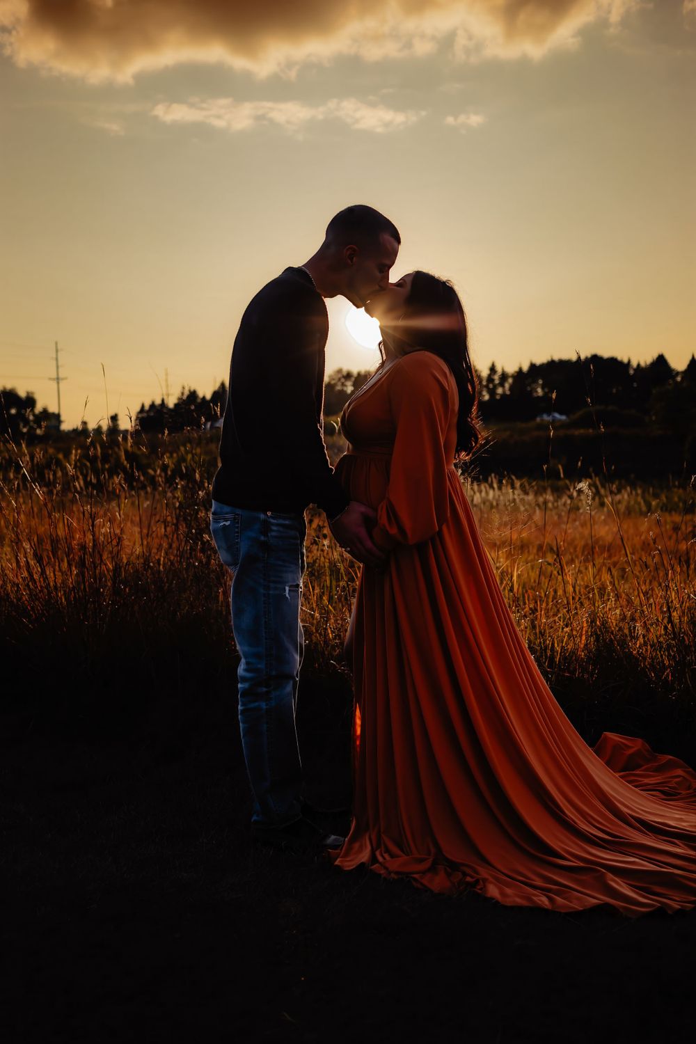 Romantic silhouette of couple in field during sunset with flowing rust-colored dress.