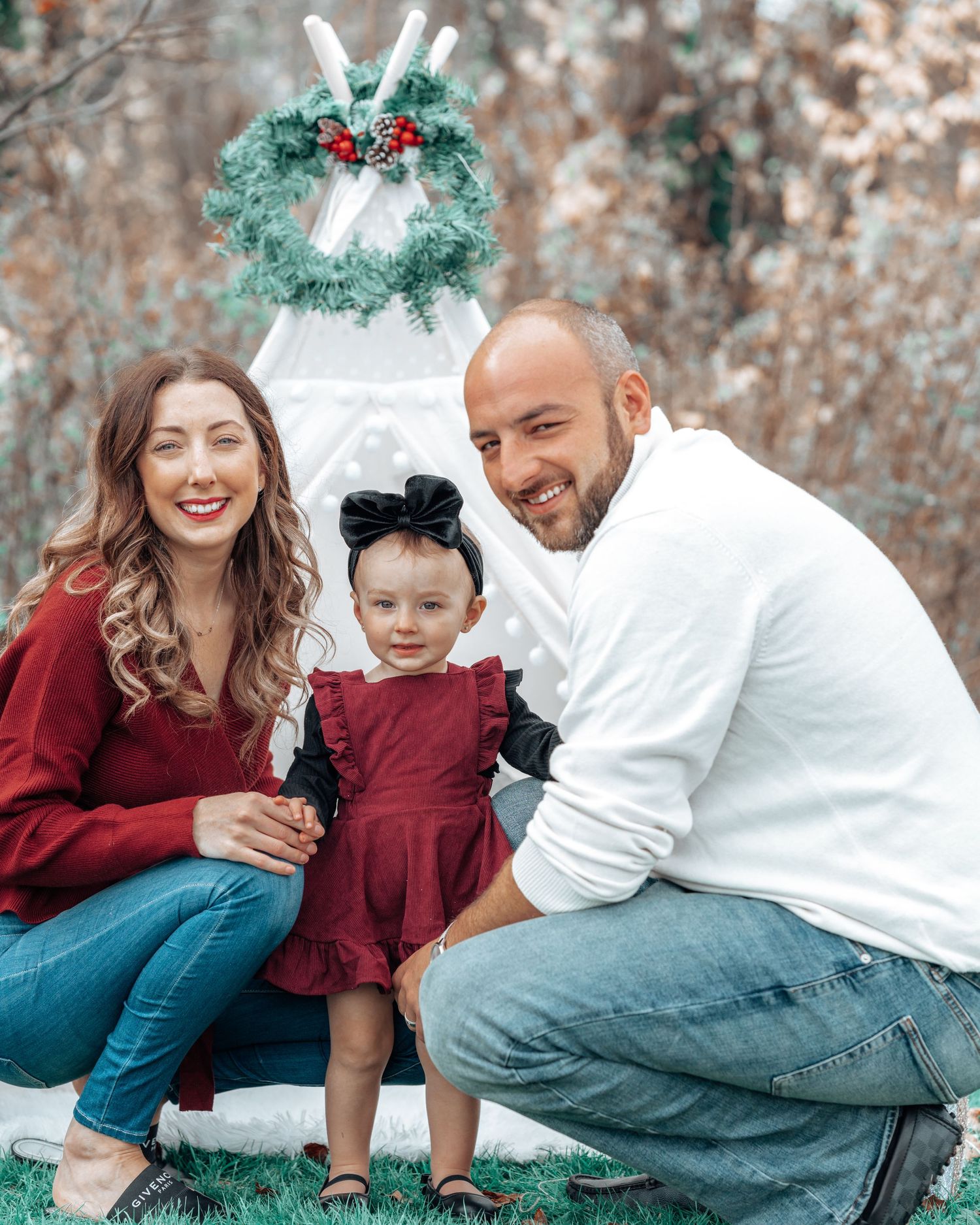 Holiday family photo setup with white teepee tent and green wreath with red berries.