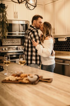 Romantic moment in modern kitchen with wine and charcuterie board on counter.