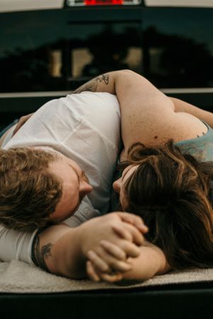 Couple lying close together in the back of a pickup truck showing affection.
