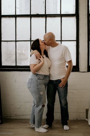 A romantic couple sharing a tender moment in front of an industrial window.