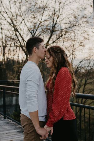Couple in red and white sharing tender moment on wooden bridge during sunset.