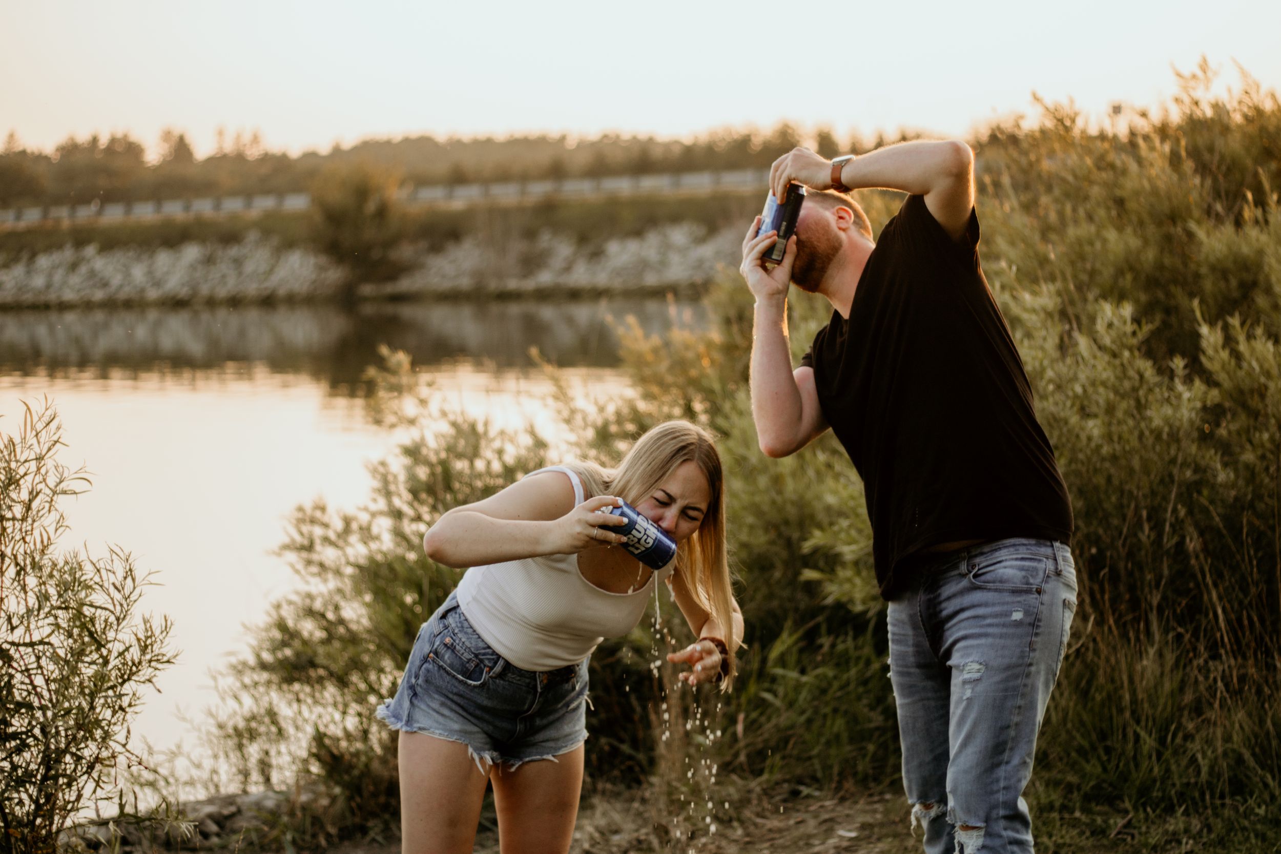 A playful couple laughs together near a waterfront during golden hour.
