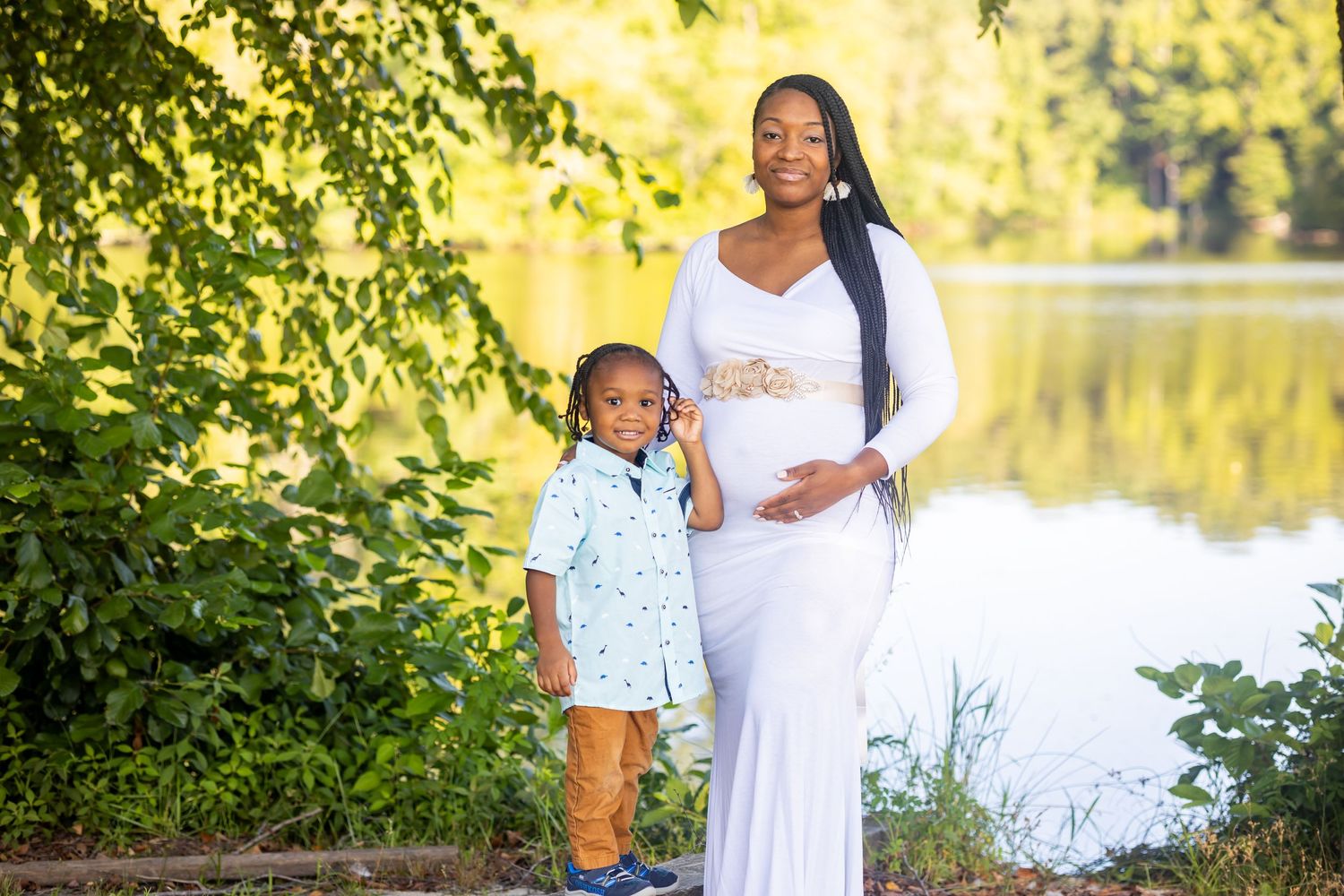 Maternity portrait of parent and child standing by peaceful lake.