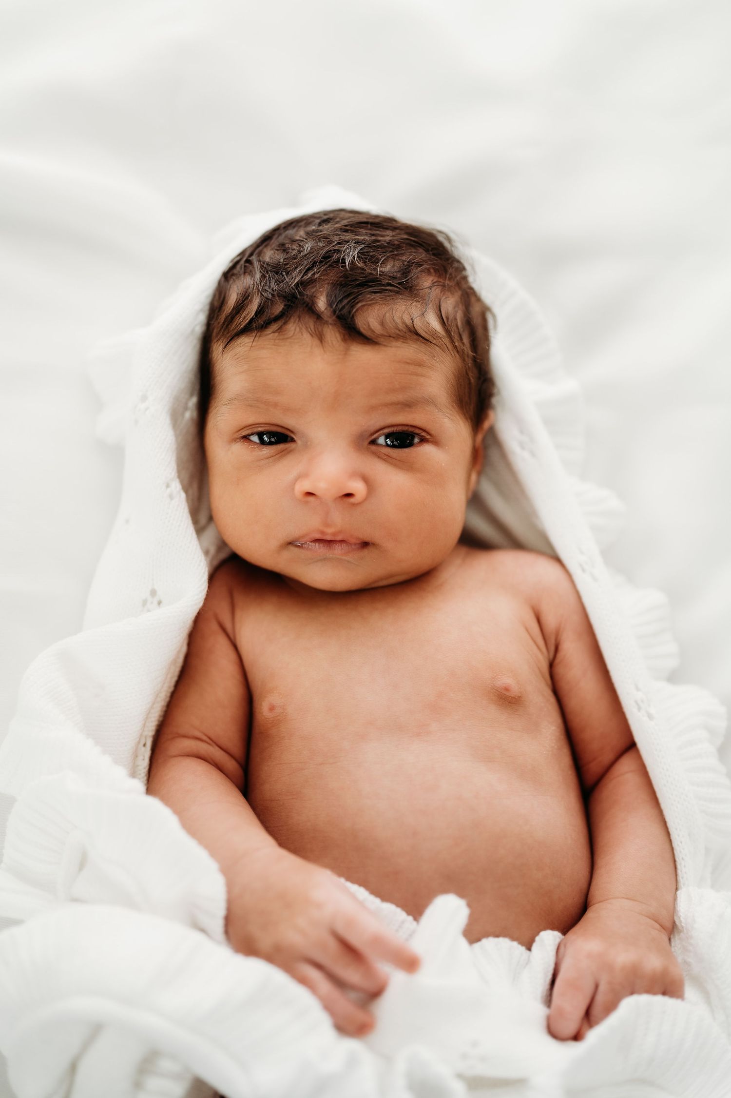 Classic white image of a newborn baby comfortably wrapped in a crisp white baby blanket