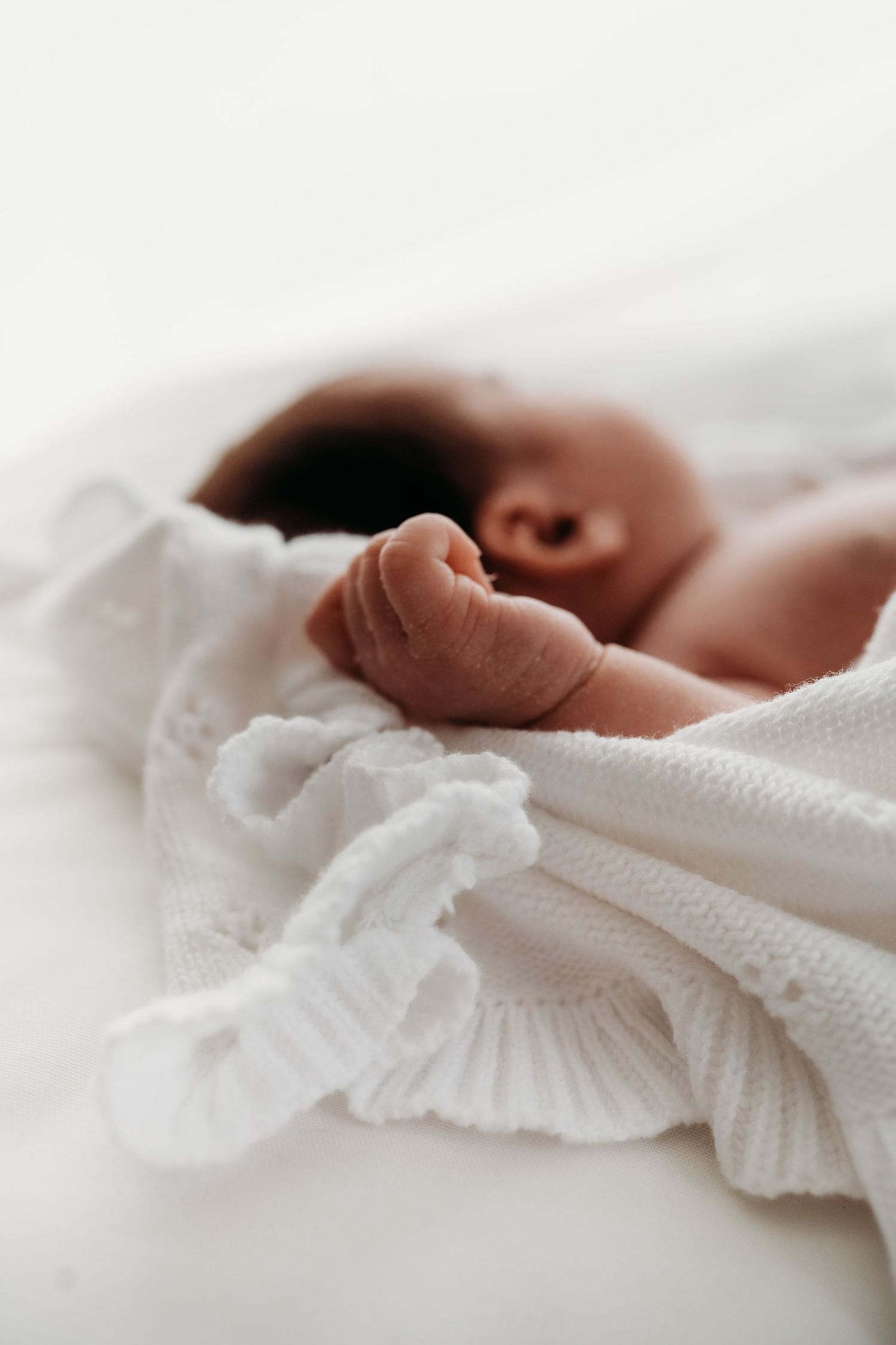 Crisp-white image of a newborn baby's hand on a white blanket