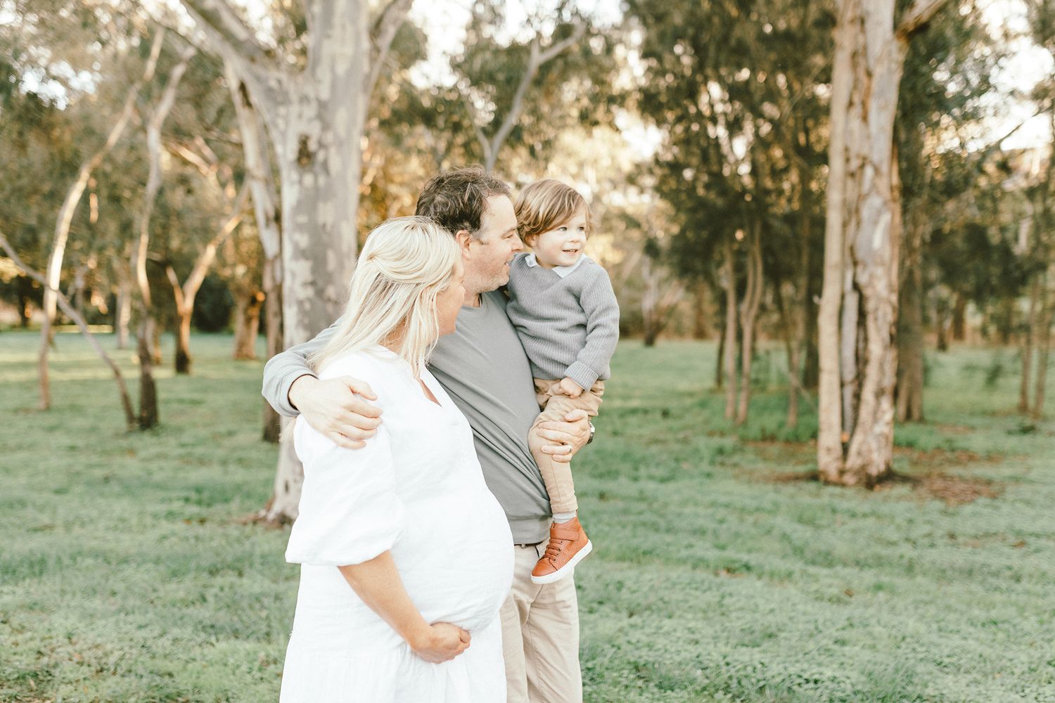 A tender maternity photoshoot captures intimate moments between a couple in natural outdoor setting.