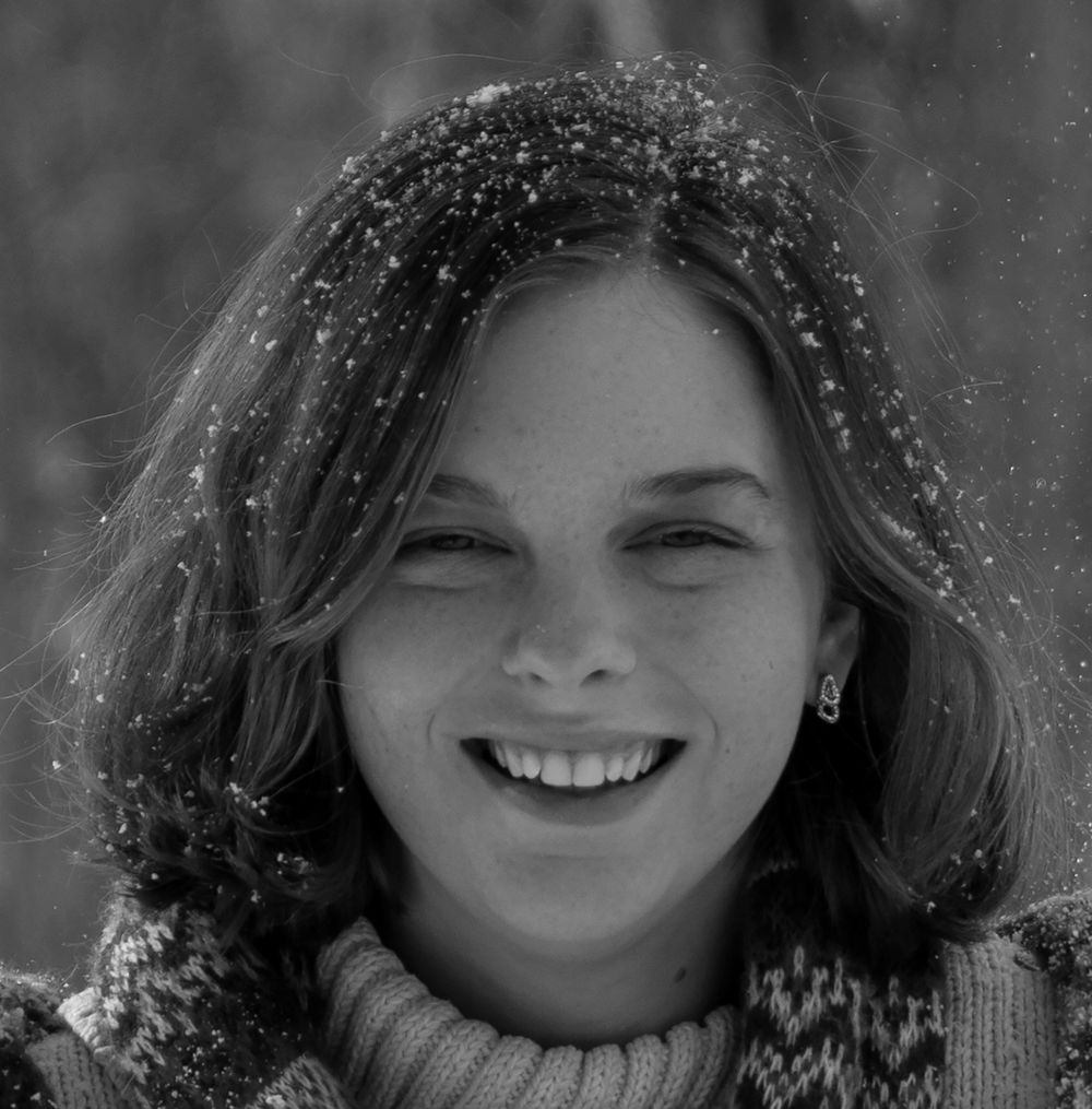 Black and white winter portrait with snowflakes falling on dark hair and genuine smile.