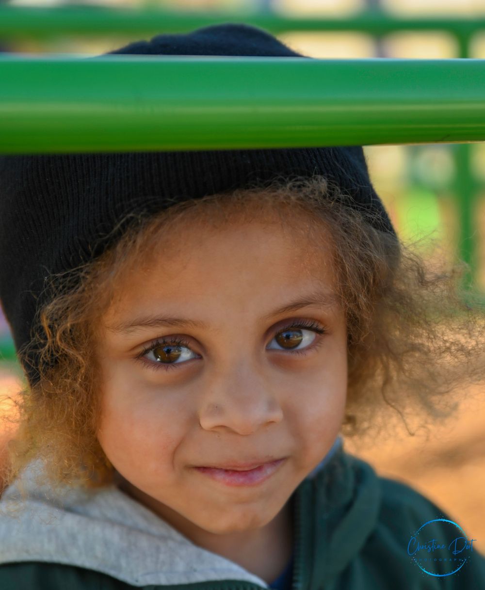 Candid portrait through green playground equipment showing bright eyes and natural smile.