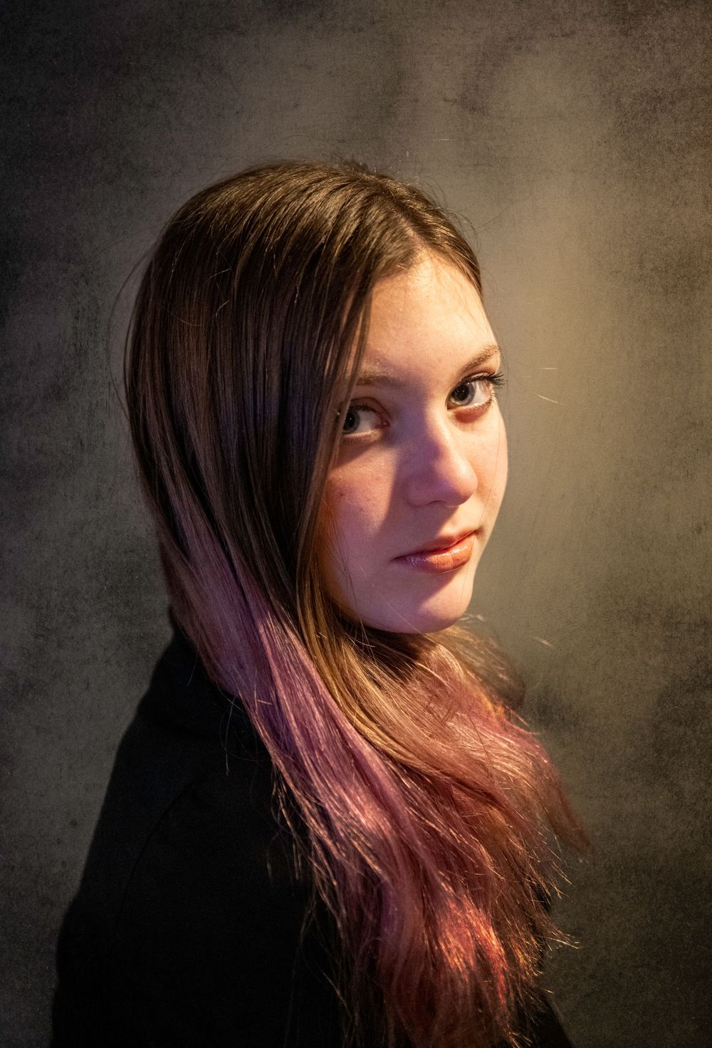 Moody portrait with dramatic side lighting showing long hair with purple tints against dark background.