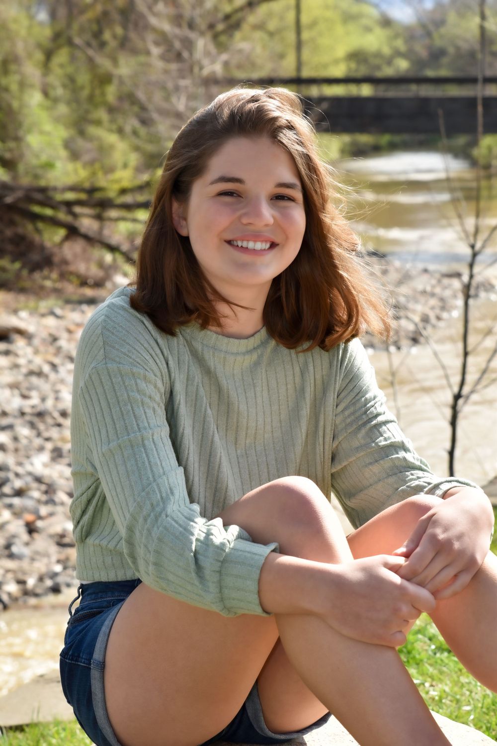 Casual outdoor portrait by a river wearing mint green sweater and denim shorts.