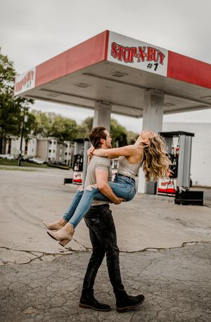 A romantic couple spins and dances together under a gas station canopy.