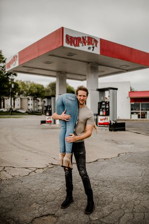A playful moment captured as a couple poses creatively at a retro gas station.