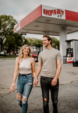 A cheerful couple shares laughter while walking at a retro Stop-N-Buy gas station.