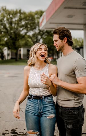 A happy couple shares a candid laughing moment outside a retro gas station.