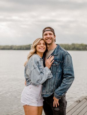 Couple in matching denim jackets share a romantic moment on a lakeside dock.