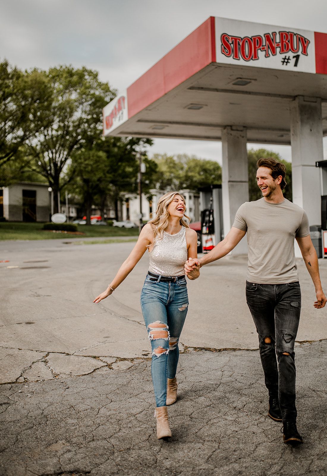 A couple strolls together with carefree expressions at an old-fashioned gas station.