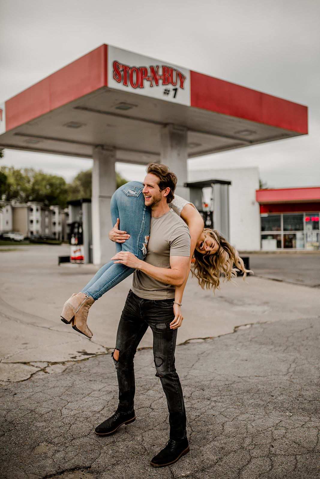 A couple plays and spins around playfully at a vintage gas station.