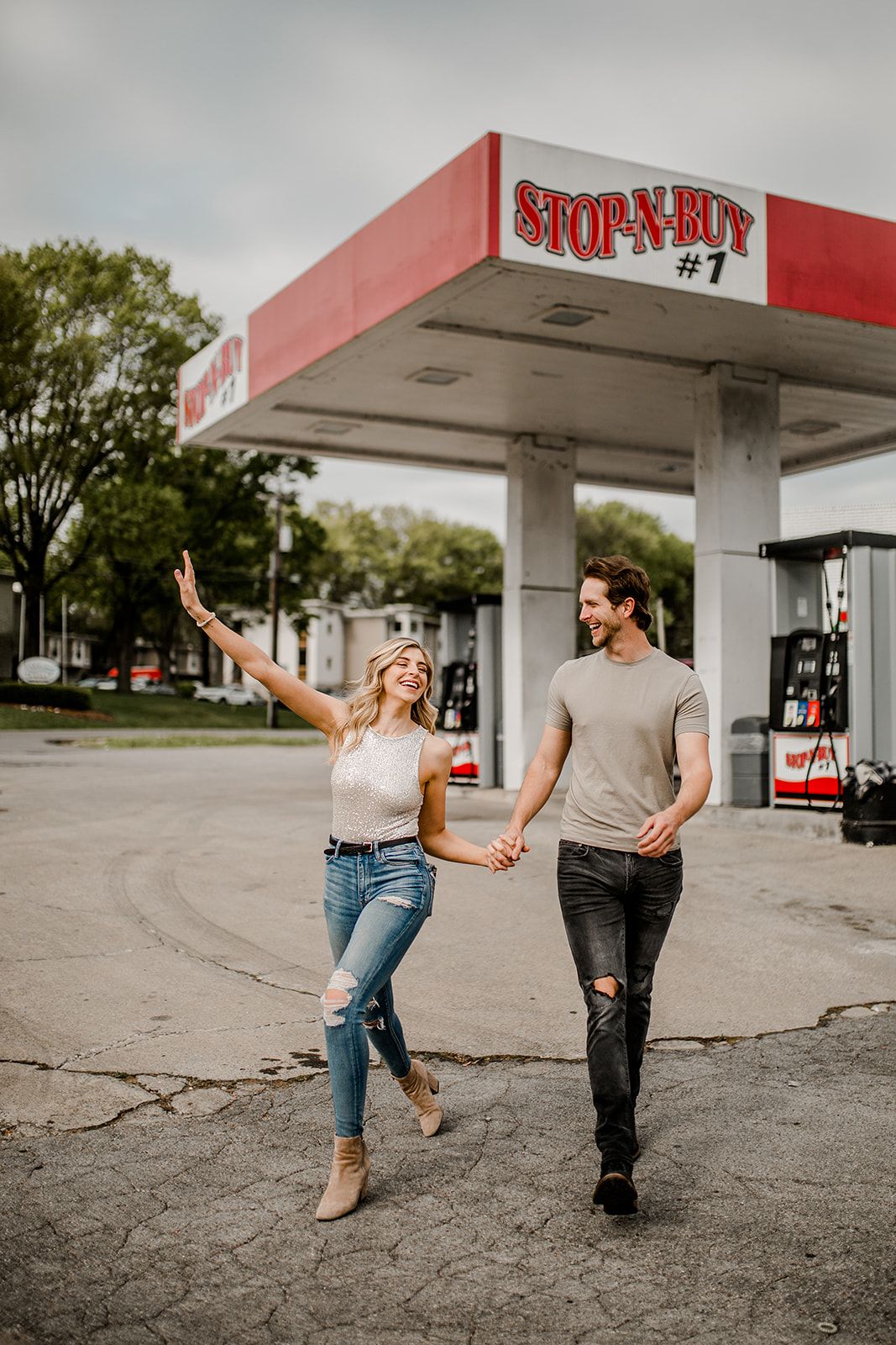A playful couple dances and walks hand in hand at a vintage Stop-N-Buy gas station.