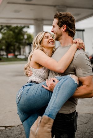 A joyful couple embraces and laughs together under a gas station canopy.