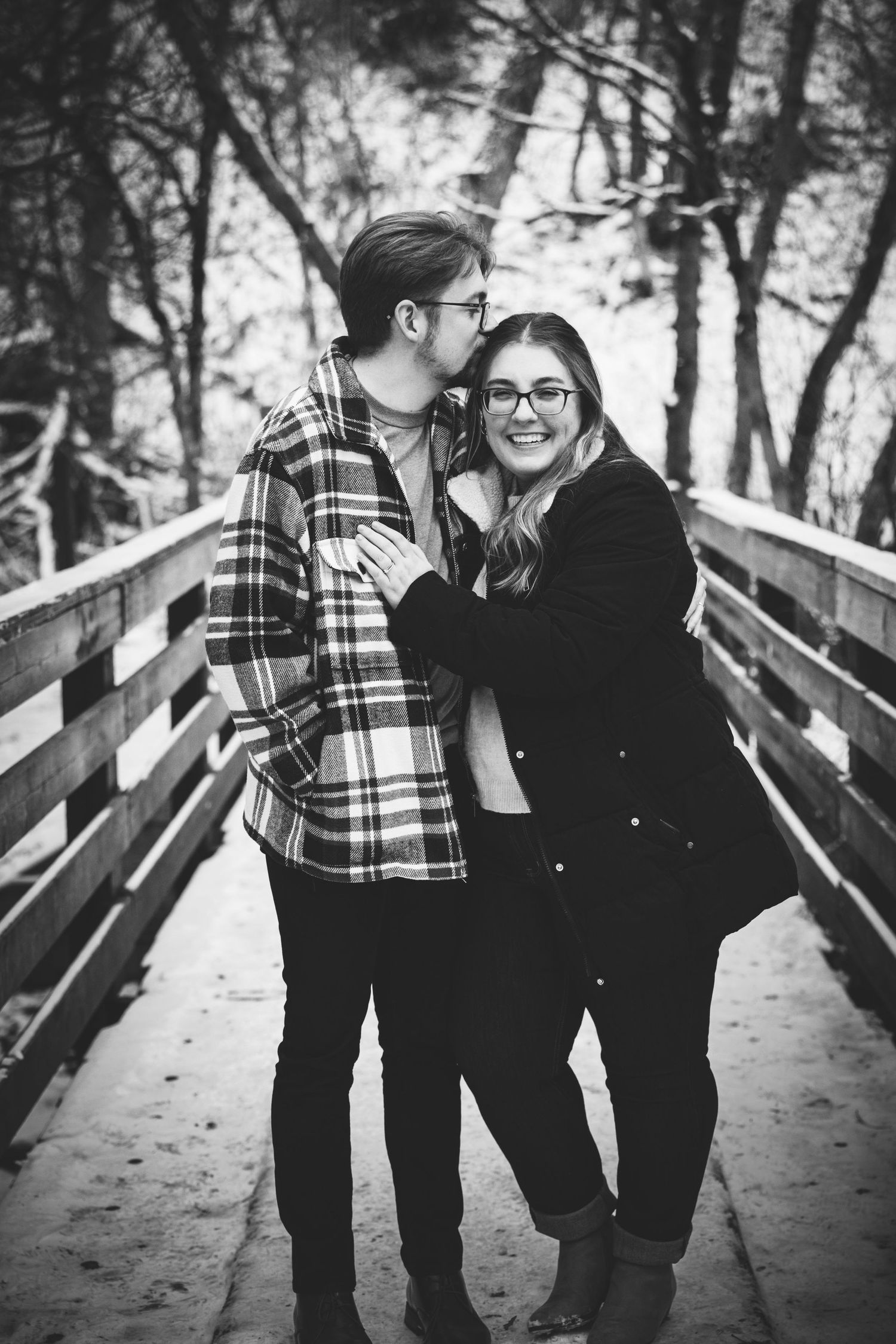 young couple standing on a bridge in the winter embracing after engagement marriage proposal