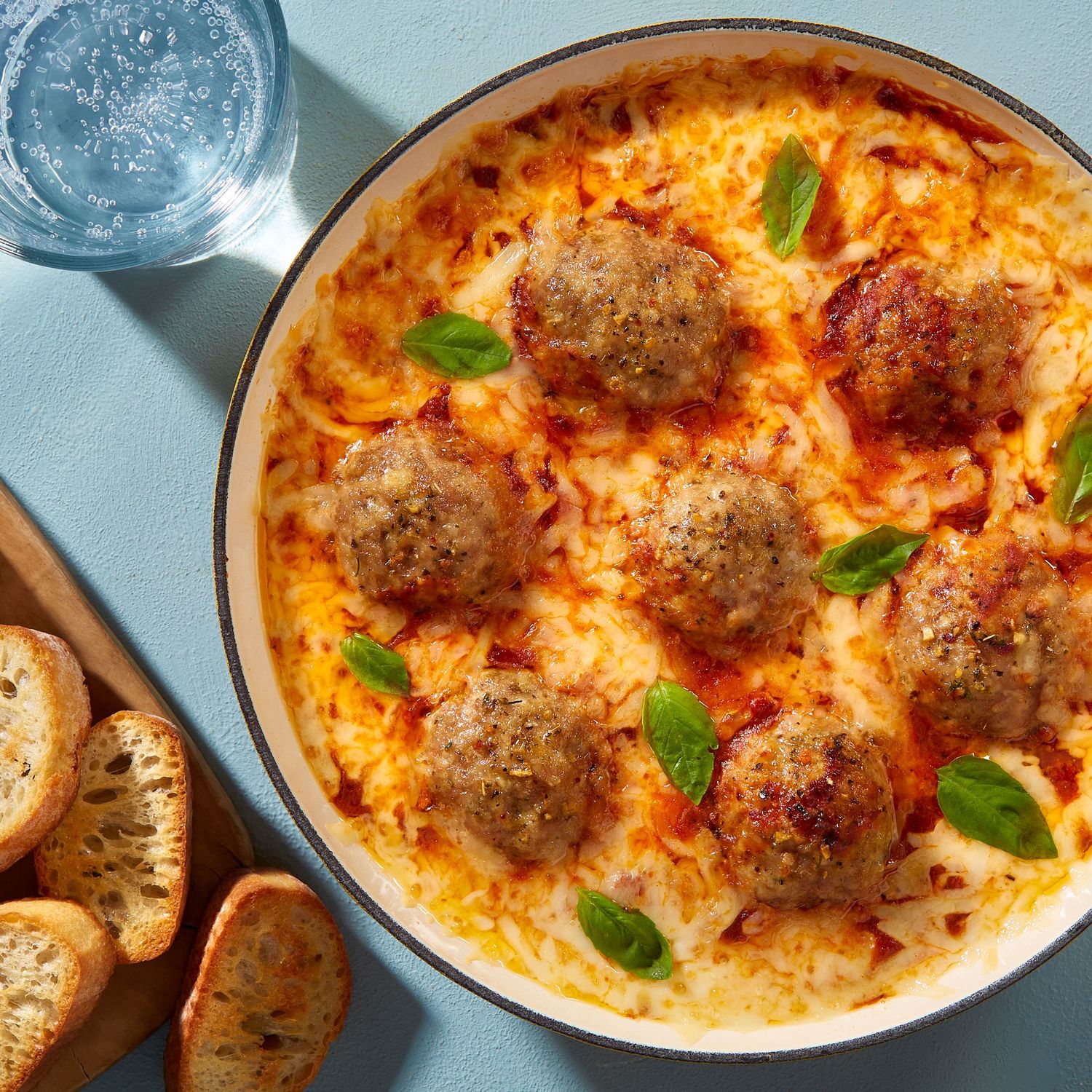 Creamy pasta bake with meatballs and melted cheese, topped with fresh herbs in a ceramic dish.