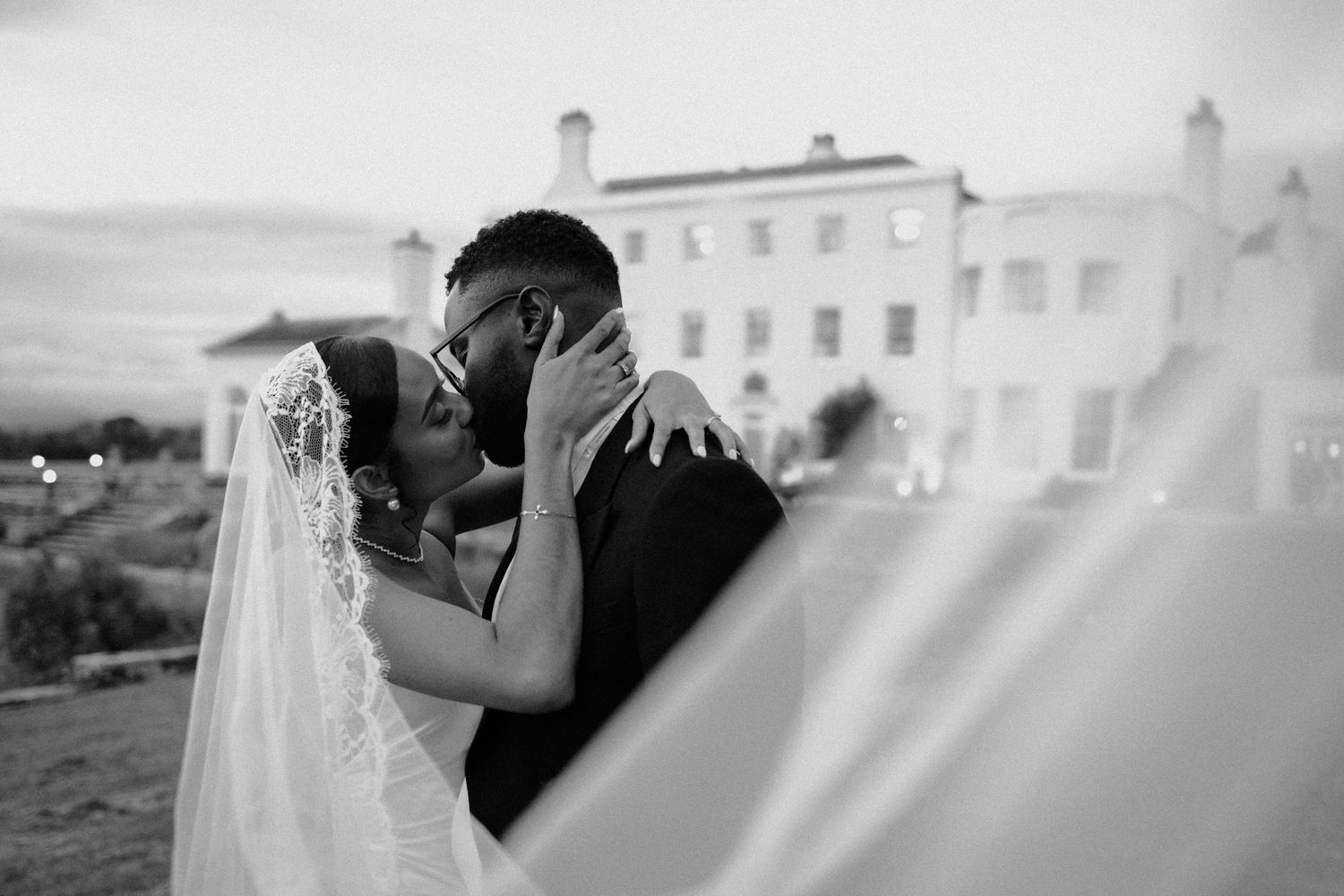 Intimate black and white portrait of couple sharing tender moment with veil in foreground.