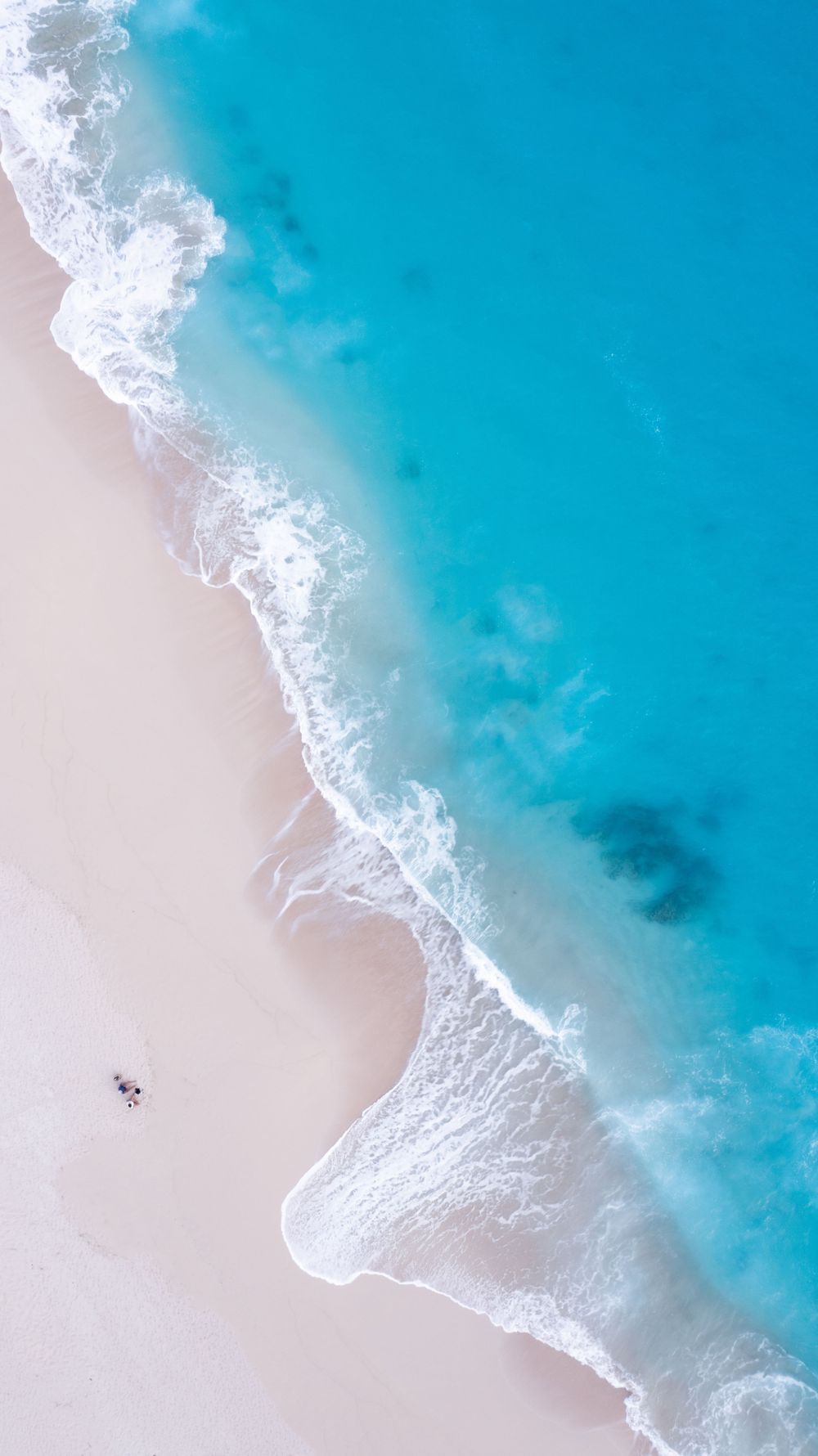 Aerial view of pristine white sandy beach meeting crystal clear turquoise ocean waters.