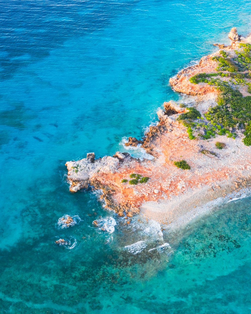 Drone shot of orange coastal cliffs and pristine turquoise Mediterranean waters.