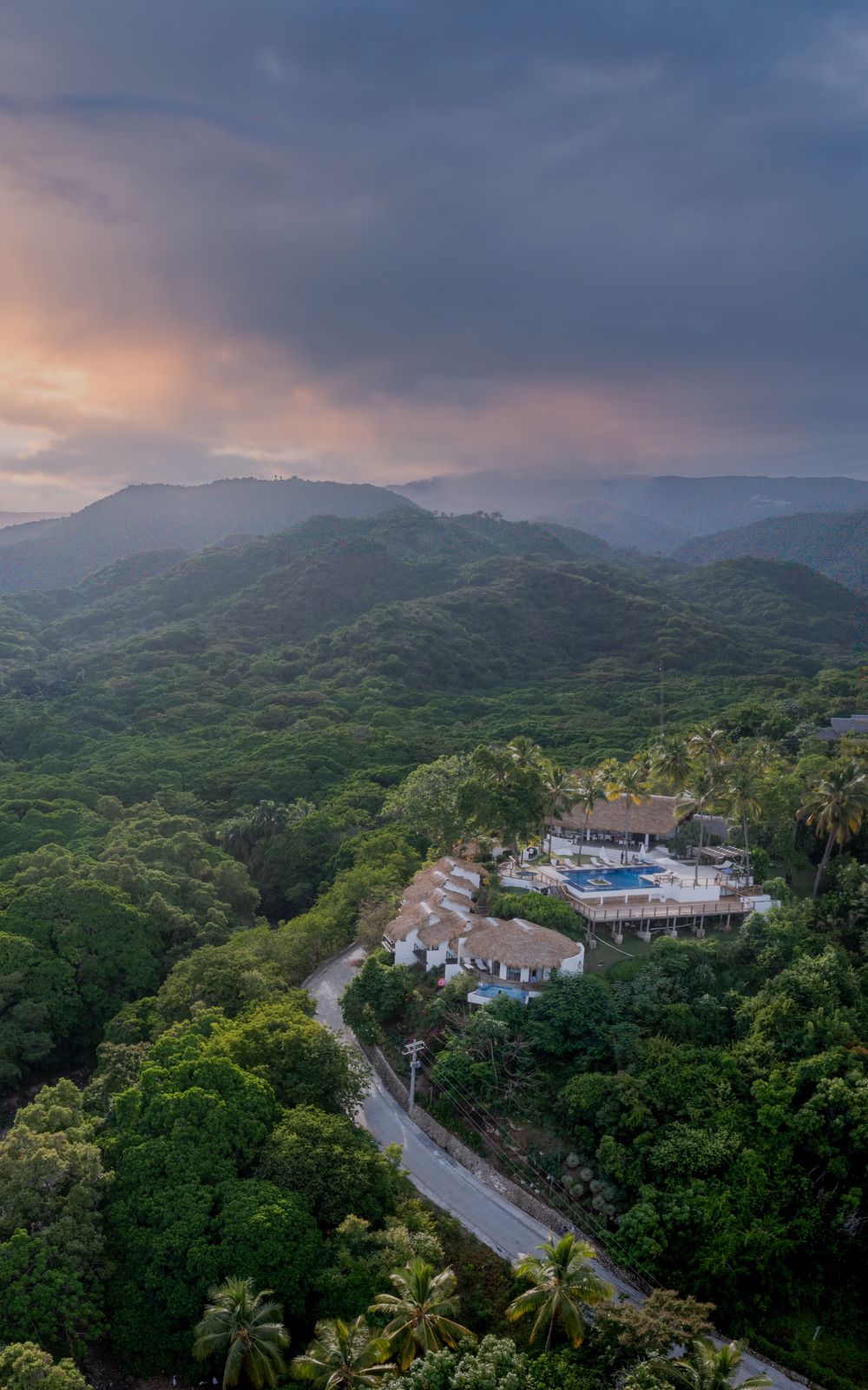 Sunset view of winding mountain road with resort buildings nestled among lush tropical forest.