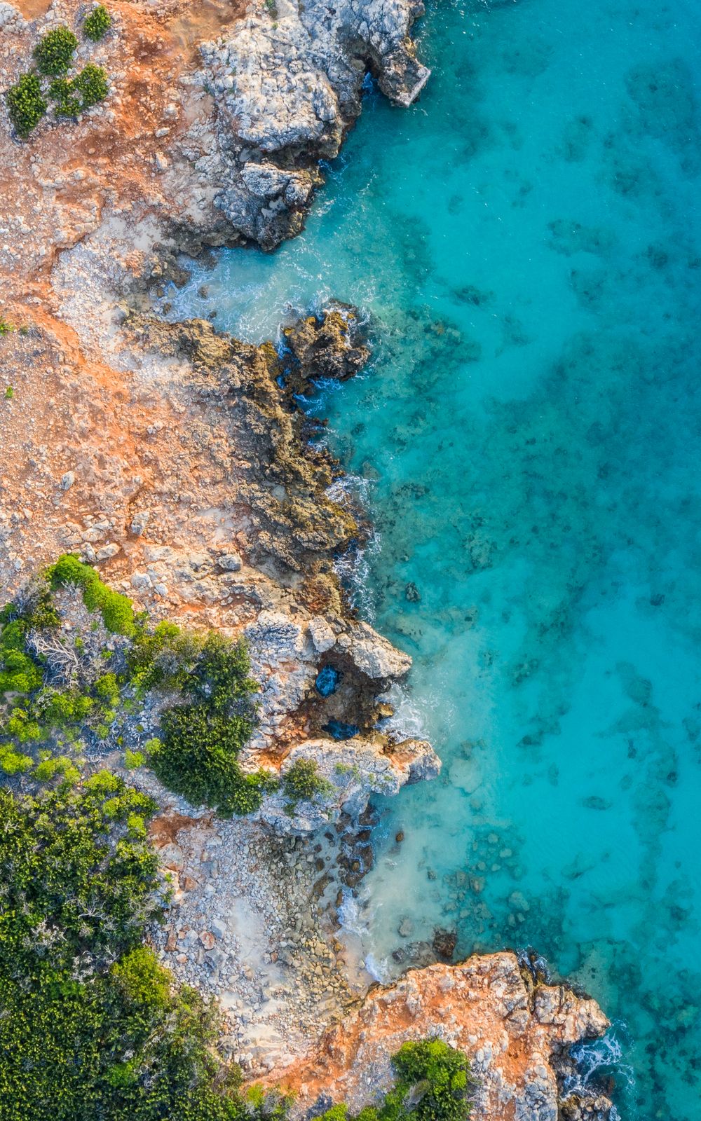 Aerial view of rugged coastline with orange rocky cliffs meeting crystal clear turquoise waters.