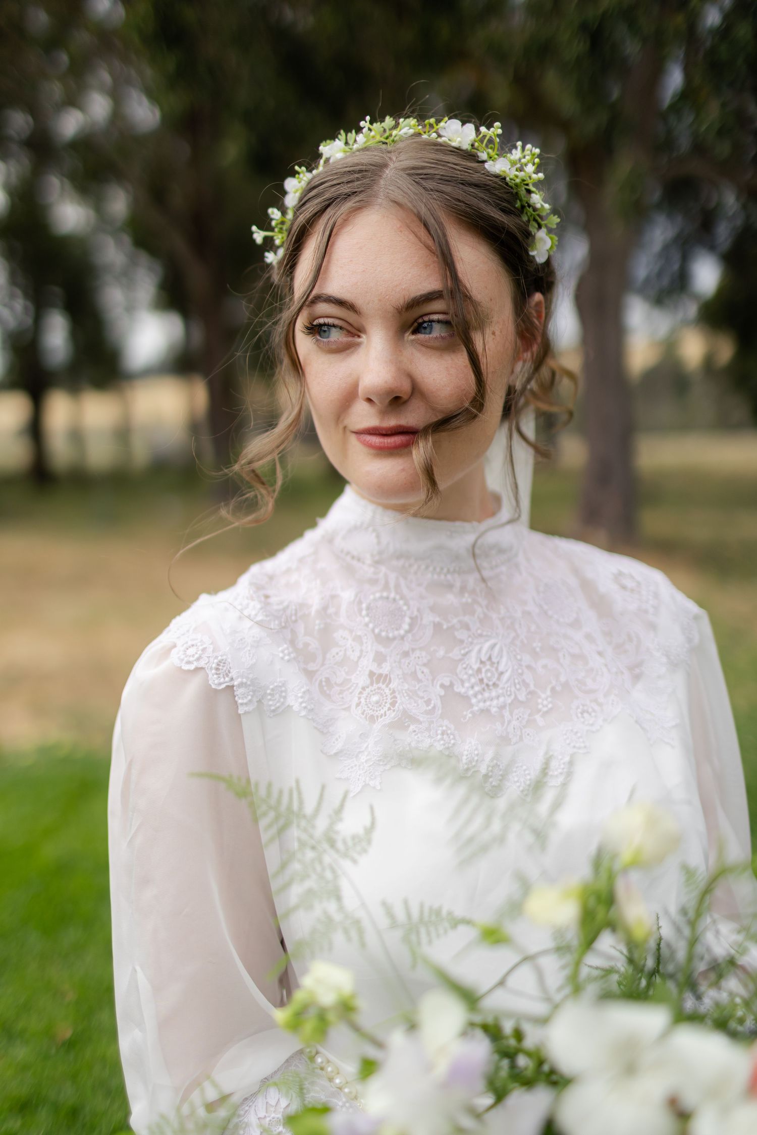 Ethereal bridal portrait featuring delicate lace dress and floral crown in outdoor setting.